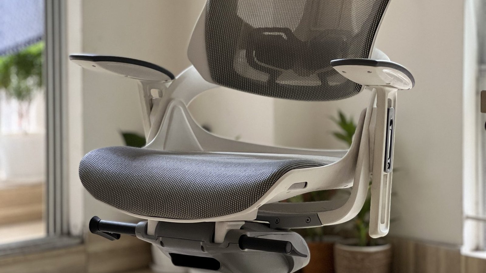Close-up of a gray ergonomic office chair showing its flip-up padded armrests and mesh seat