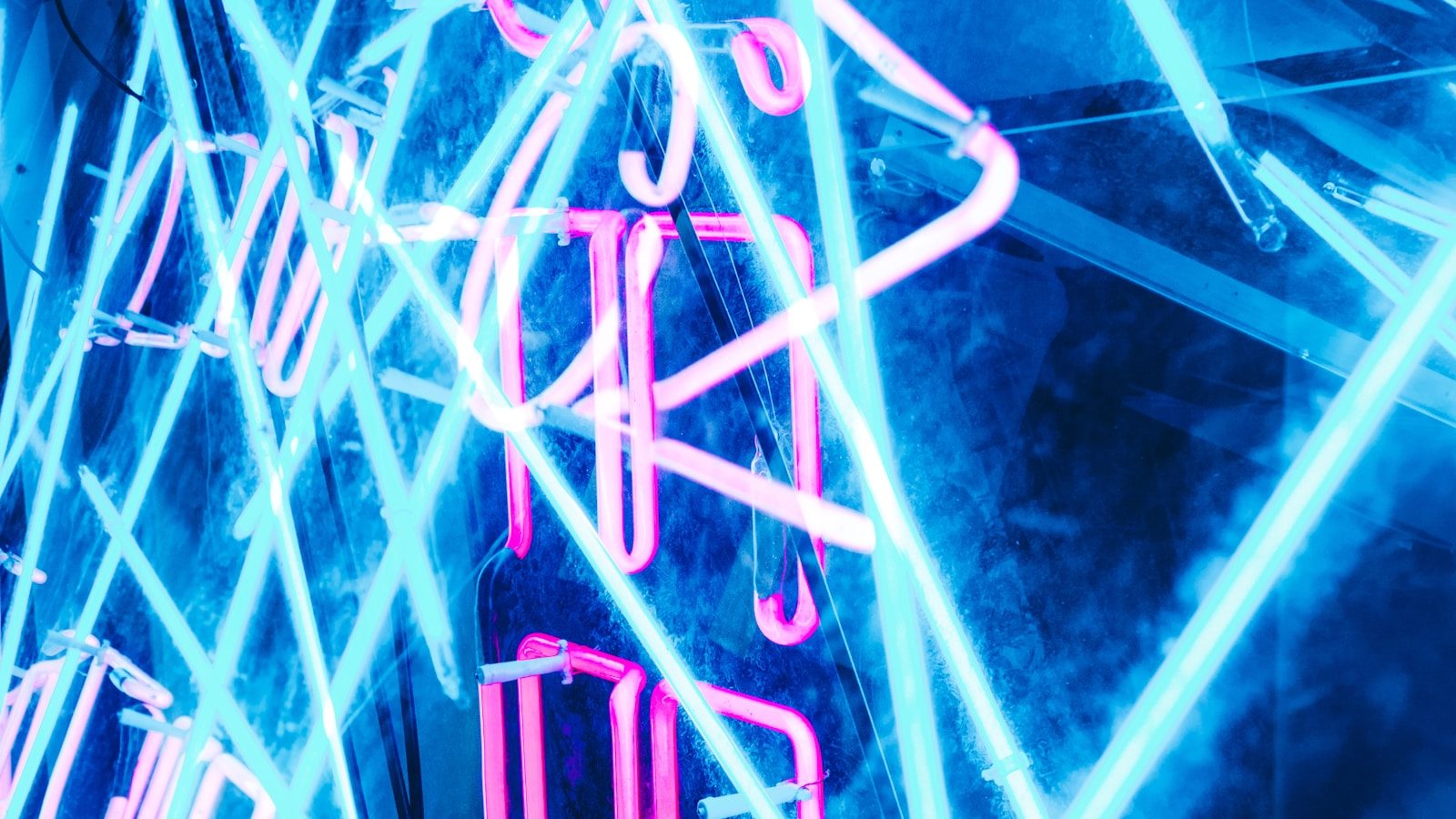 Crossed pink and cyan neon light tubes glowing against a dark blue background