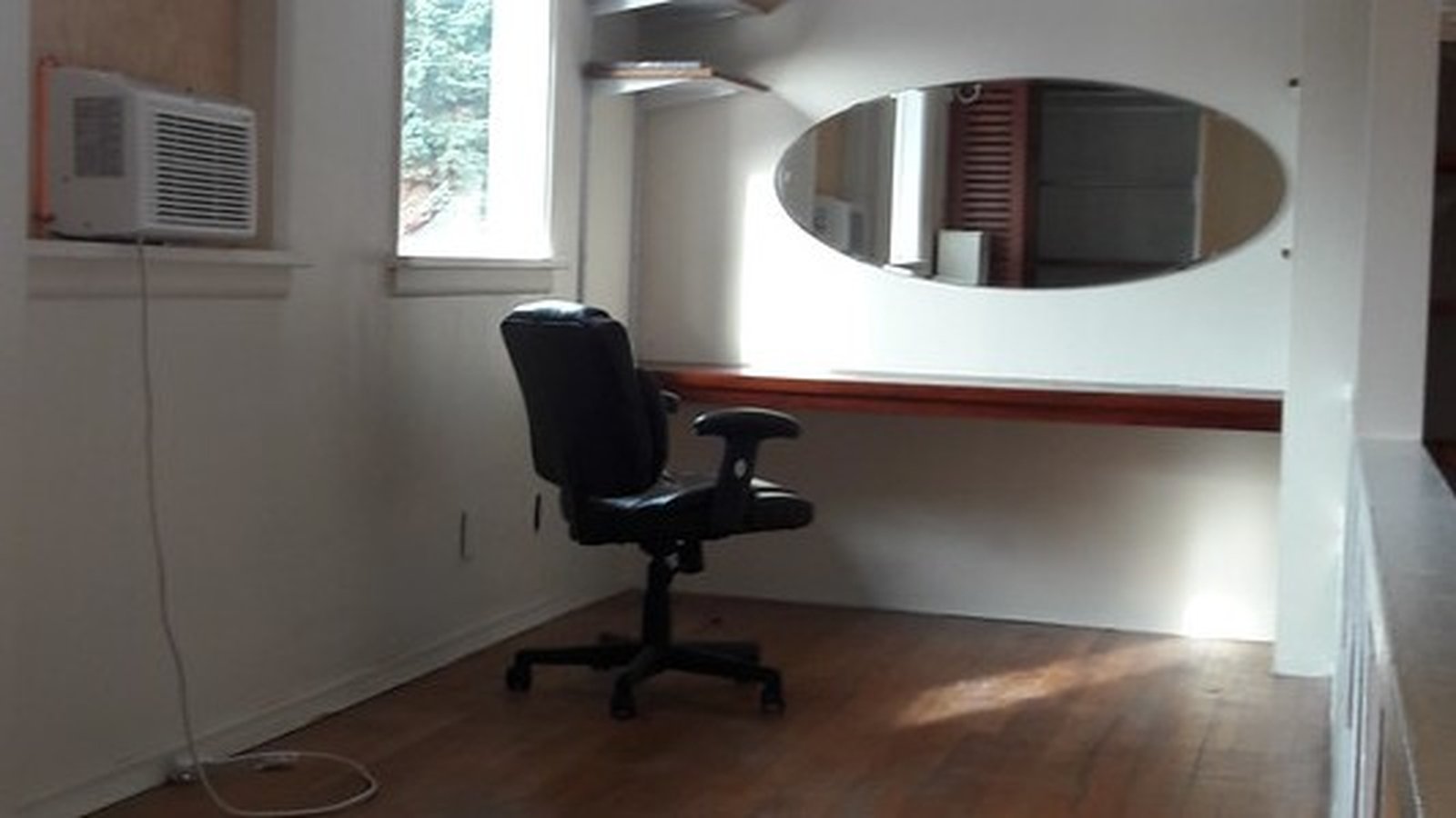 An empty black office chair beside a built-in desk shelf under a window