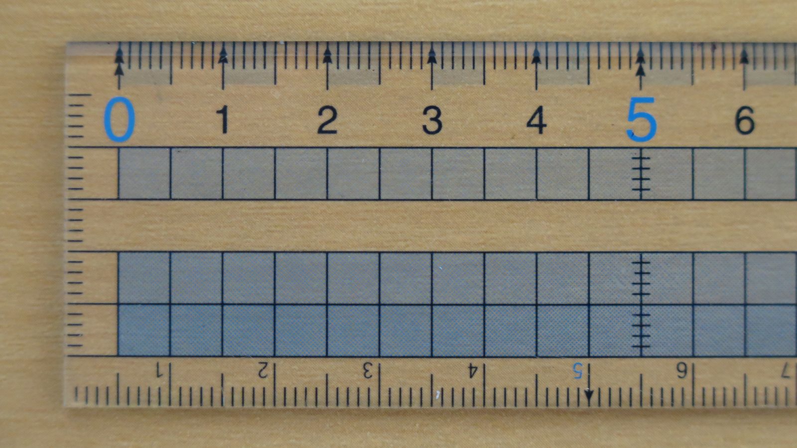 A clear plastic ruler resting on a light wood table, marked in inches and centimeters