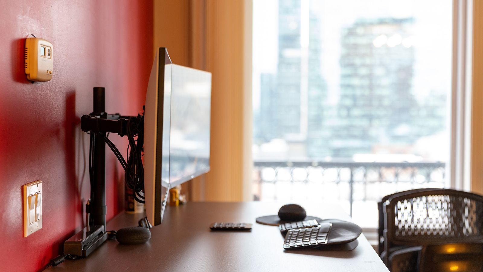 A monitor held on an articulating VESA arm mount, seen edge-on, clamped to the back of a desk