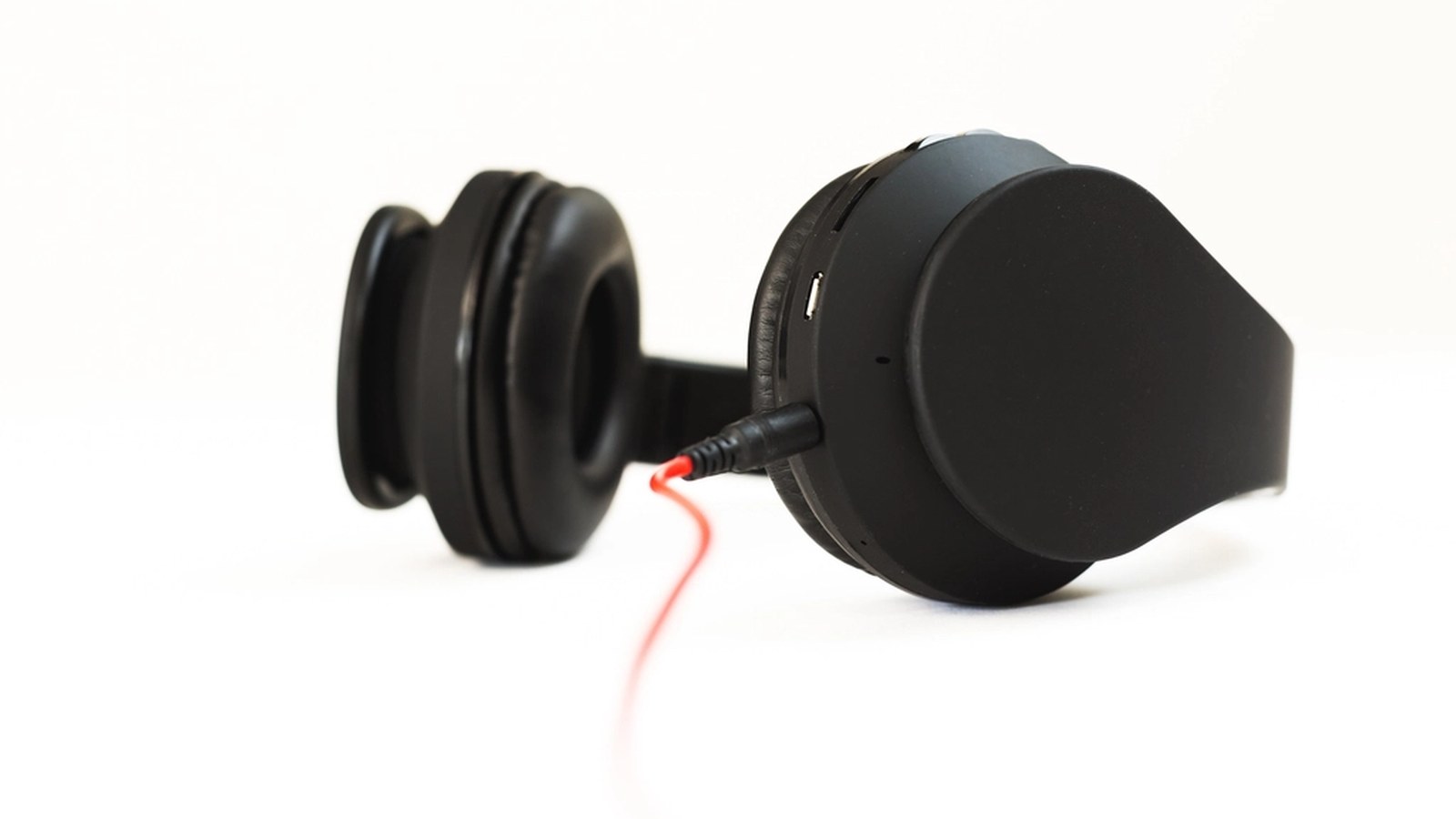 Black over-ear headphones with a red cable, resting on their side against a plain white background