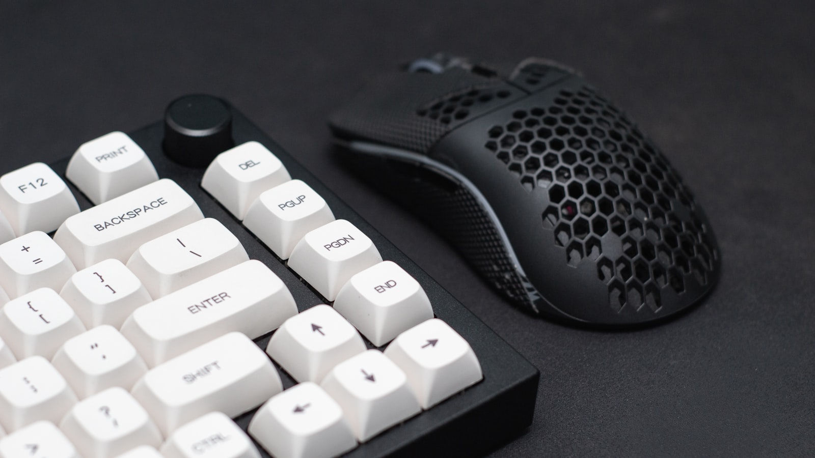 A white mechanical keyboard and a black honeycomb-shell gaming mouse on a dark desk surface