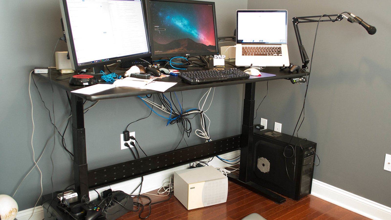 A desk with dual monitors, a laptop and a scissor microphone boom arm clamped to the far edge