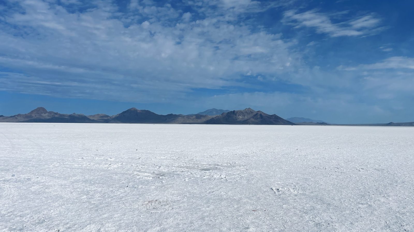 A flat white salt desert stretching to a line of distant mountains under a blue sky