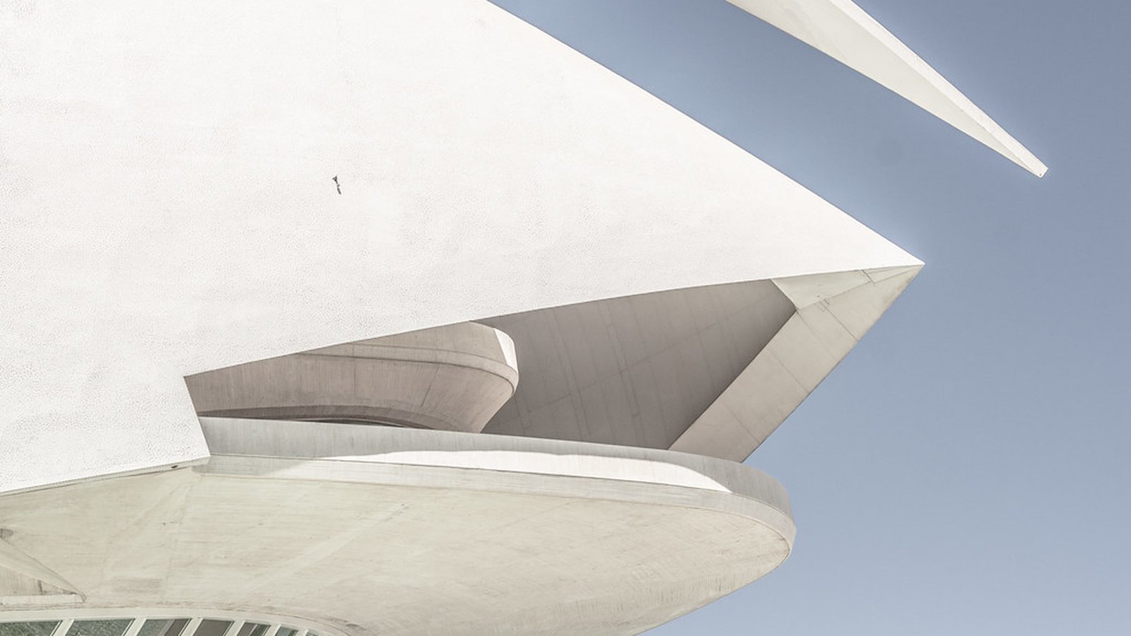 A curved white concrete building roofline against a clear blue sky