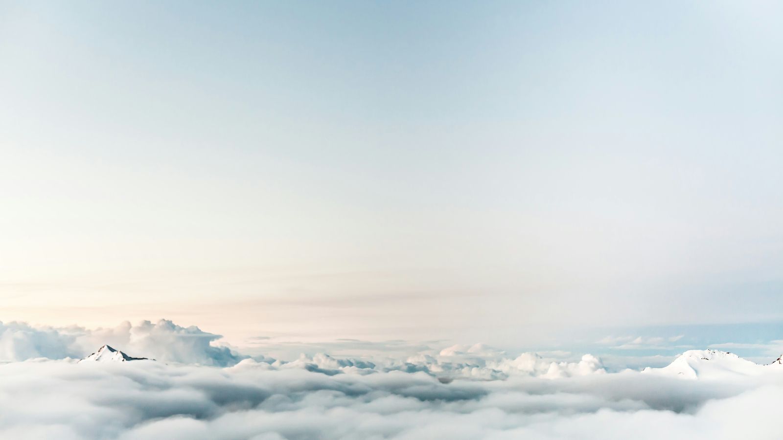 Mountain peaks rising above a pale sea of clouds at dawn