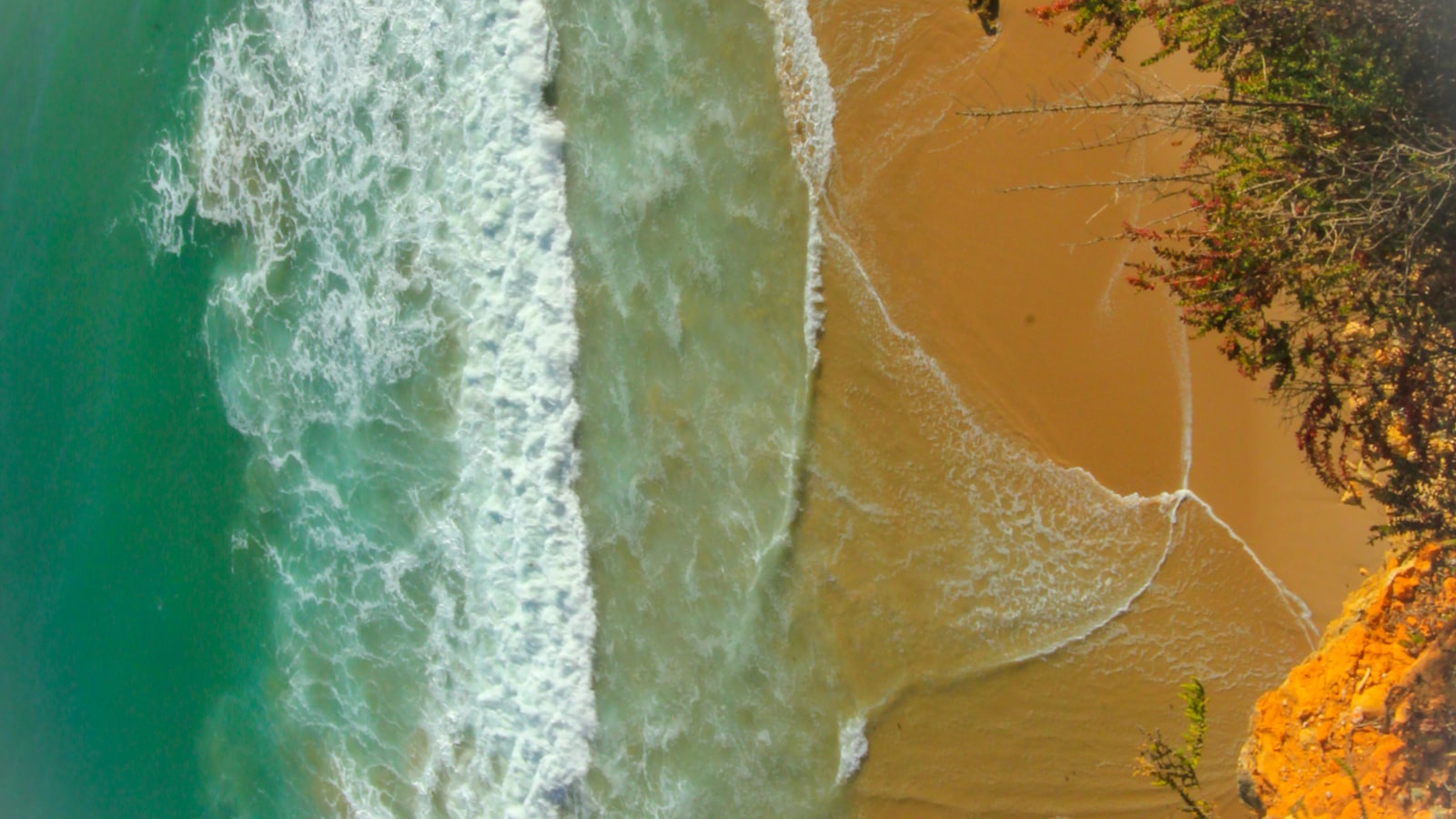 Aerial view of turquoise ocean waves meeting a sandy beach