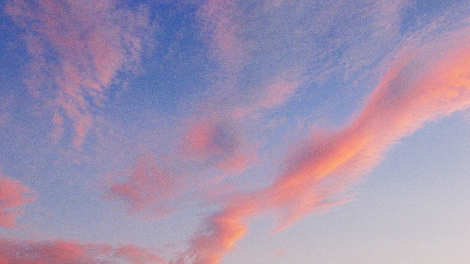 A periwinkle blue sky streaked with soft coral-pink clouds at dusk