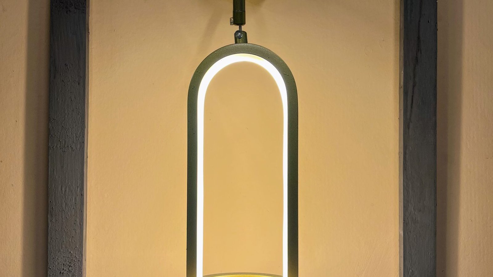 A glowing arched LED light fixture mounted on a wall in a dim, warm-lit room