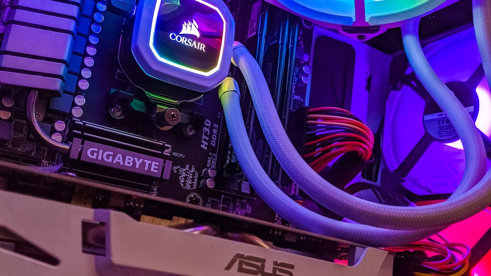 Close-up inside a PC case with blue and purple RGB lighting on a liquid cooler, motherboard, and braided cable sleeving