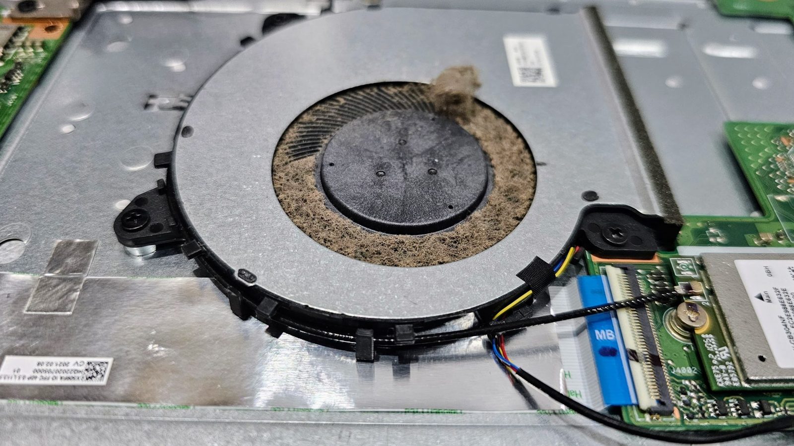 An opened laptop showing its cooling fan with a thick ring of dust packed around it