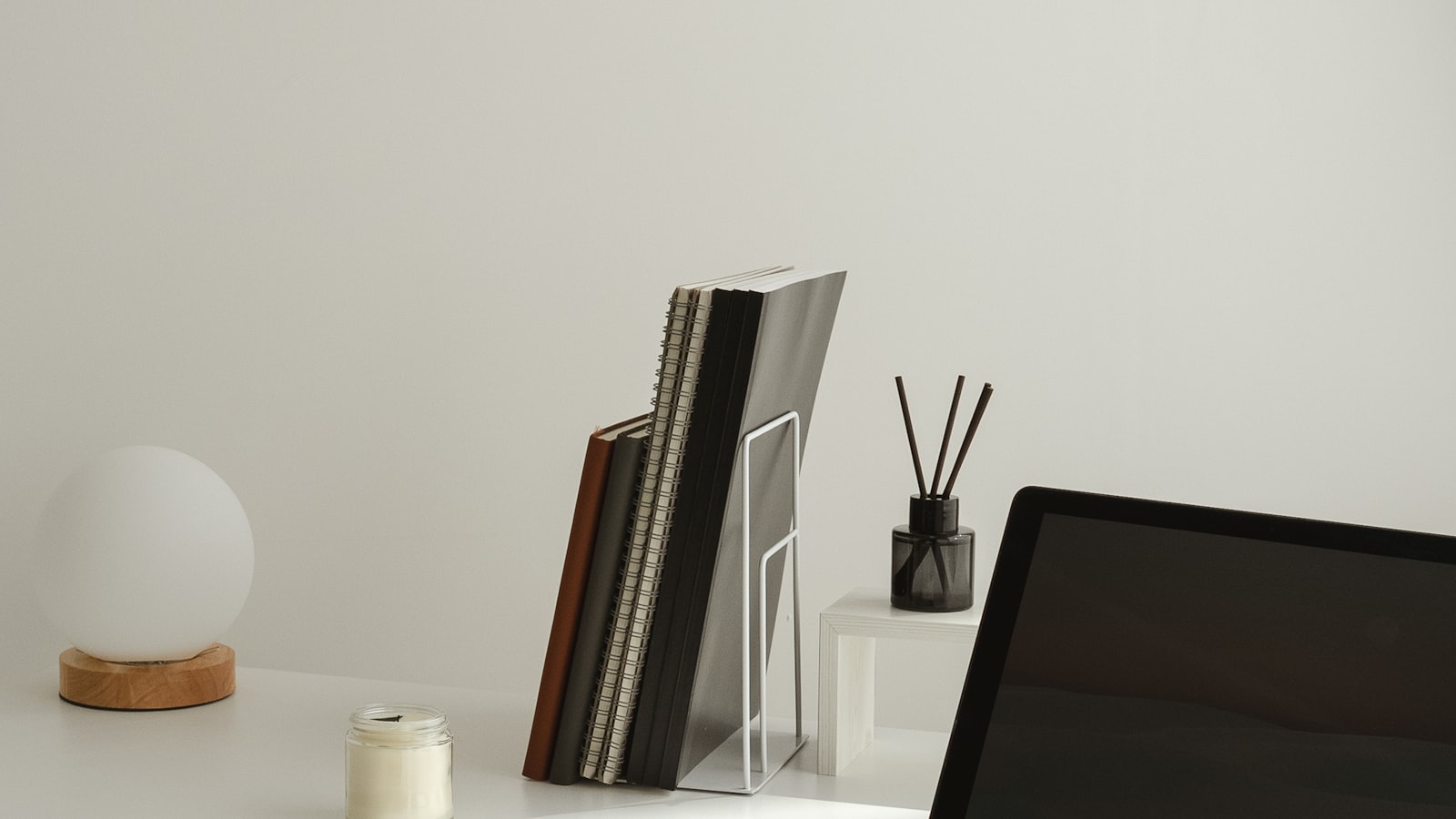 A minimalist white desk with a small riser block, a spiral notebook stand, and a laptop edge visible