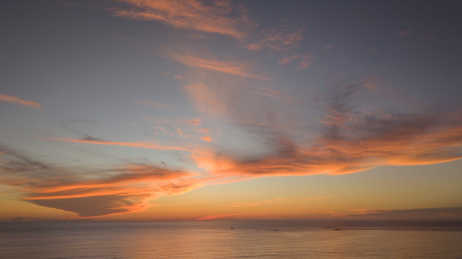 Streaks of orange and pink cloud across a blue-gray sky above a calm ocean horizon at dusk