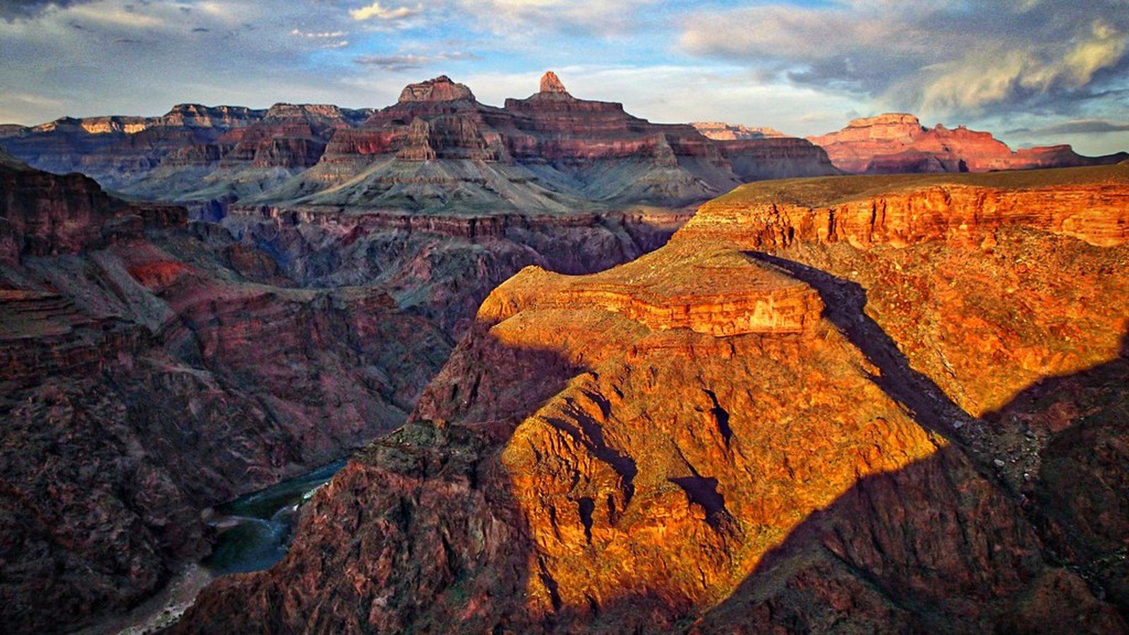 Golden-hour light striking a canyon ridge in orange and rust tones under a blue sky with scattered clouds