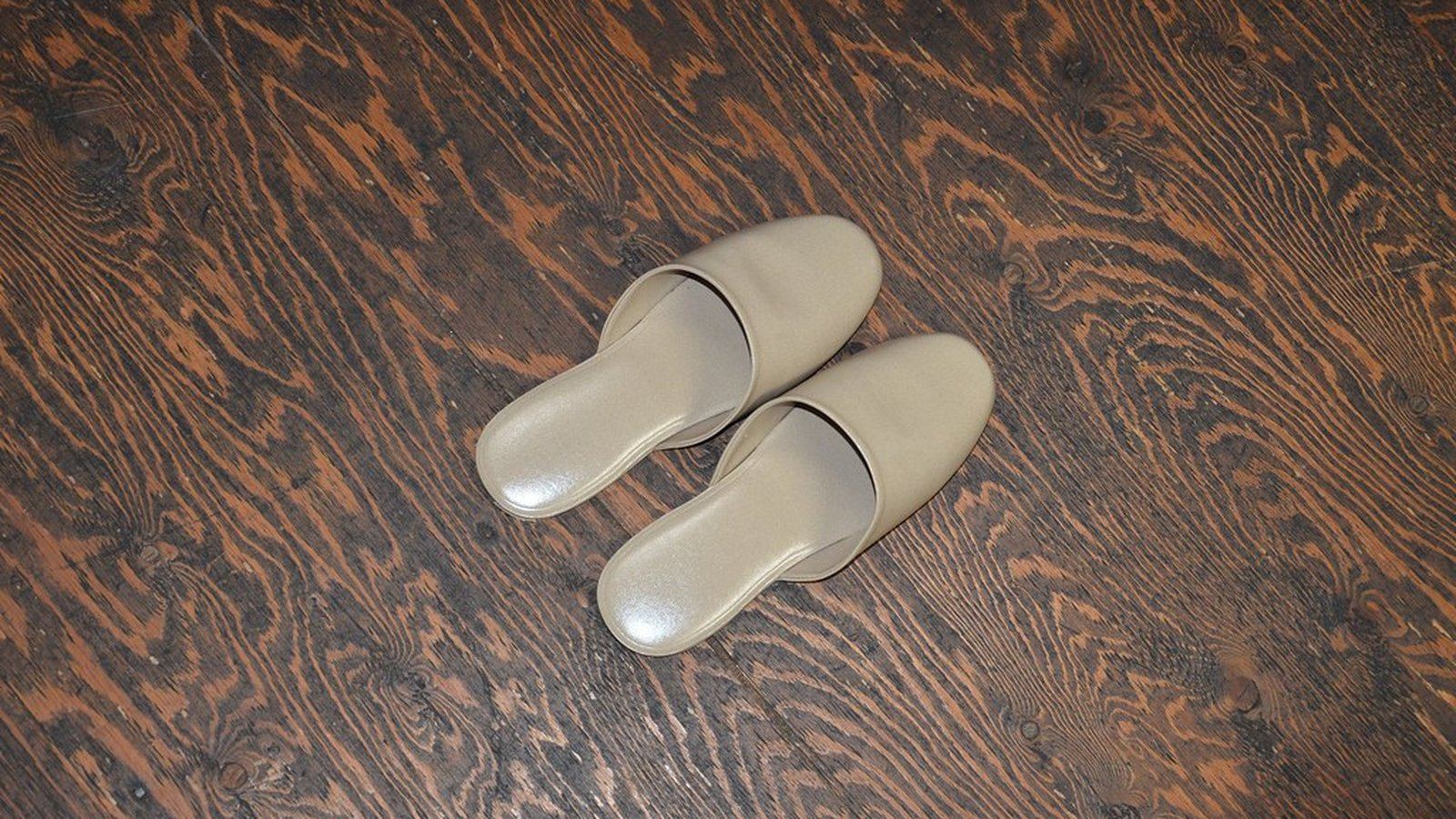A pair of slippers resting on a dark wood floor, viewed from above
